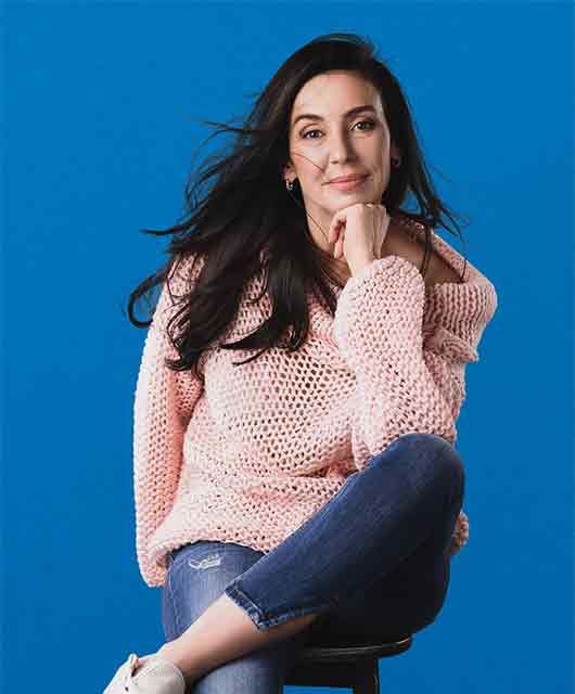 middle aged woman with dark long hair sitting on a chair looking at the camera